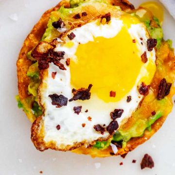 Overhead close up photo of Keto Avocado Toast with melted cheese, a fried egg, and crumbled bacon.