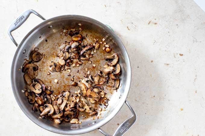 Photo of onions and mushrooms cooking in a skillet.
