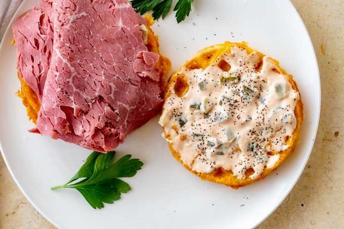 Photo of two chaffles on a white plate.  One has a keto friendly thousand island spread on it and the other has corned beef.