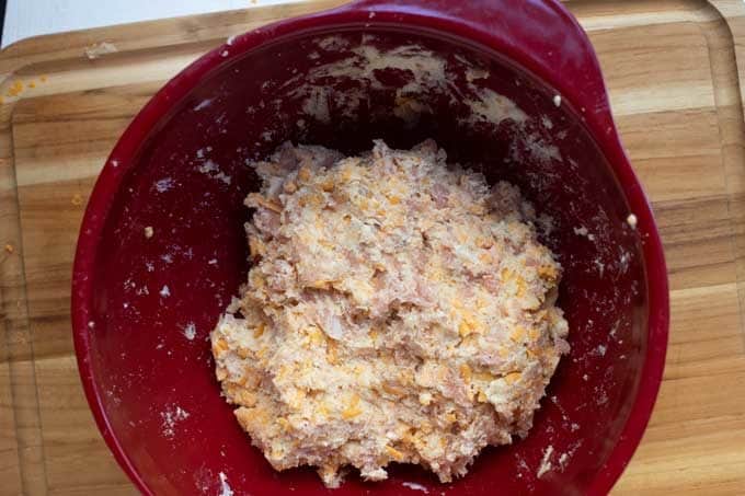 Photo of almond flour, baking powder, sea salt, ground black pepper, cayenne pepper, sausage, grated cheddar cheese, and cream cheese mixed together in a red bowl.
