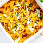 A baked Keto Chicken Bacon Ranch Casserole in a white dish, topped with melted cheddar cheese, crumbled bacon, chopped parsley, and drizzles of creamy ranch sauce.