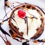 Close-up photo of a Chocolate Chaffle topped with Ice cream, chocolate syrup, pecans, and a raspberry.