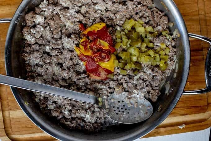 Overhead photo of a skillet of ground beef with pickles, ketchup, and mustard.