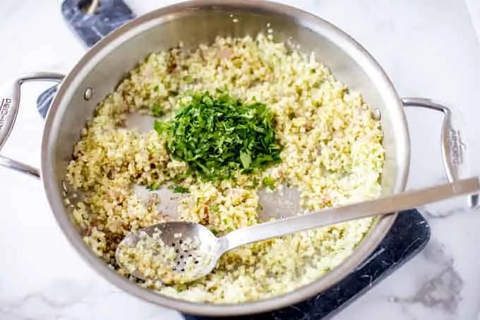 Photo of a skillet of cauliflower rice, onion, garlic, seasonings, and cilantro.