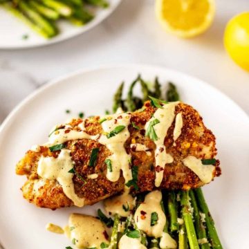 Photo of a piece of low carb Chicken Cordon Bleu drizzled in sauce sitting on a bed of asparagus.