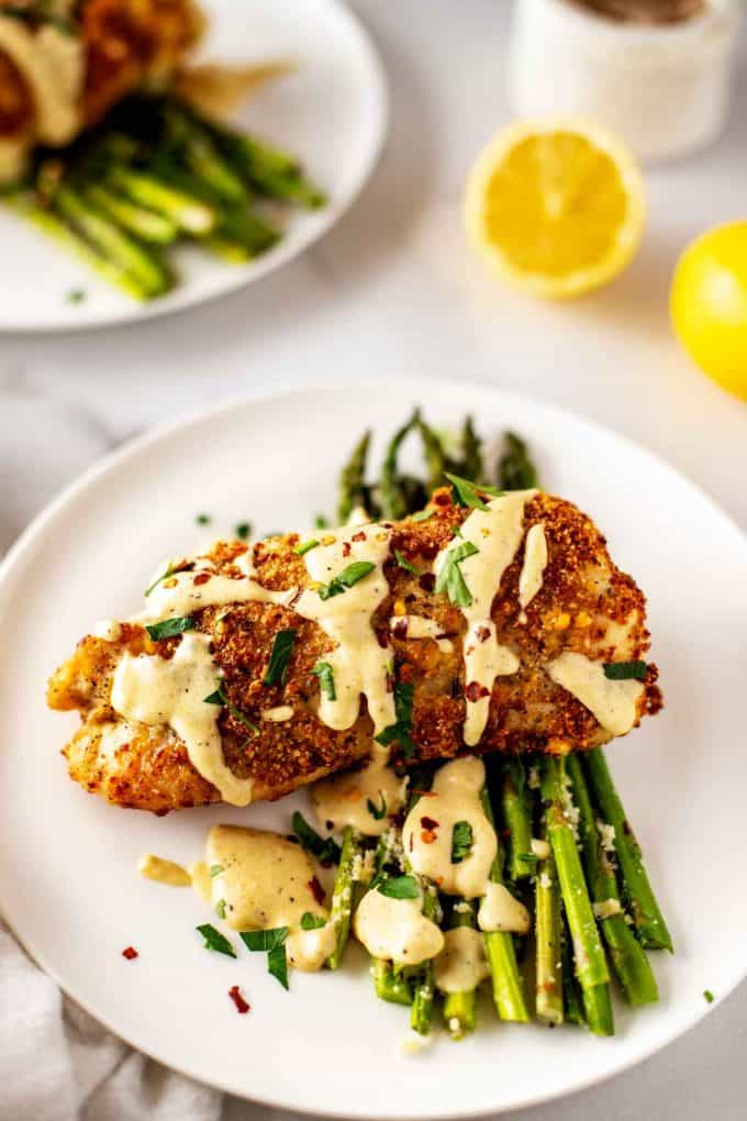 Photo of a piece of low carb Chicken Cordon Bleu drizzled in sauce sitting on a bed of asparagus.