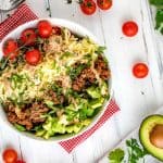 Square overhead photo of a keto taco salad surrounded by tomato, avocado, and cilantro.