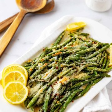 Photo of Roasted Green Beans with Parmesan on a white serving platter with wooden utensils next to it.
