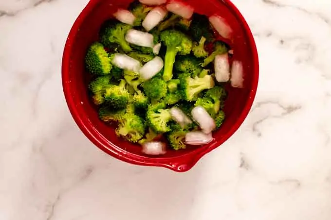 Photo of broccoli that has been blanched in a red bowl of ice water.