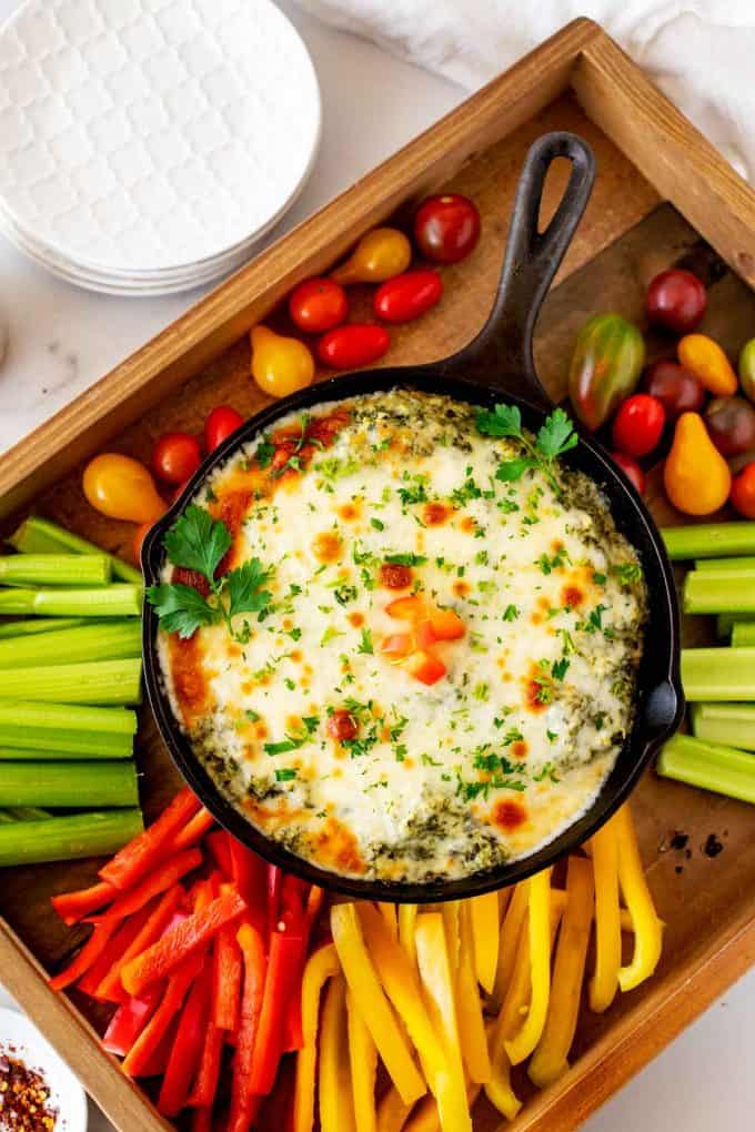 Overhead photo of Keto Spinach Dip in a cast iron skillet surrounded by vegetables on a wooden tray.