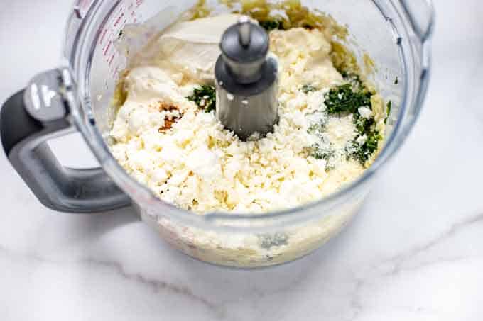 Photo of mayonaise, sour cream, spinach, parmesan, and artichokes in a food processor.