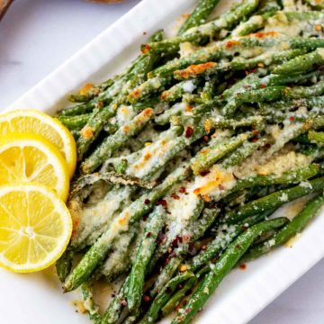 3/4 overhead photo of Roasted Green Beans with Parmesan on a white platter garnished with lemons.