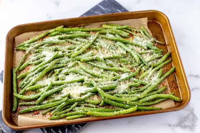 Photo of roasted green beans in a baking sheet that have had Parmesan cheese sprinkled over them.