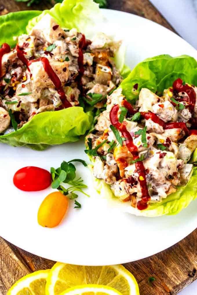 Photo of a white plate of keto chicken salad in lettuce wraps drizzled with hot sauce.