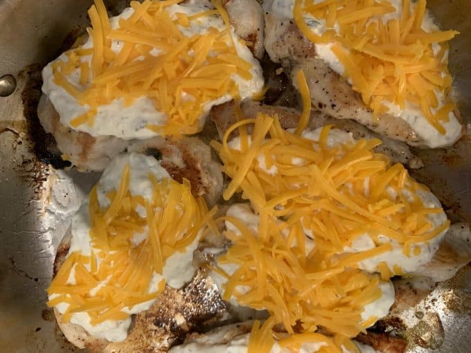 A skillet of browned chicken with cream cheese and cheese on top of it.
