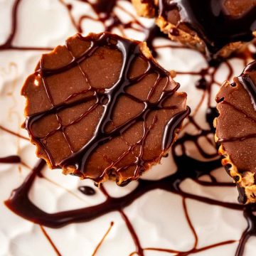 Close up square image of chocolate cheesecake fat bombs on a white plate drizzled with chocolate syrup.