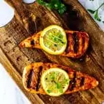 Overhead square photo of marinated chicken on a wooden cutting board garnished with lemons and microgreens.