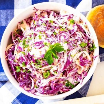 Close up overhead photo of Keto Coleslaw in a white bowl sitting on a blue and white checkered napkin.