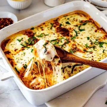 Square photo of a meatball casserole in a white casserole dish with a wooden spoon scooping out a meatball with stringy cheese.