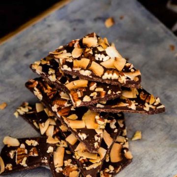 Photo of Keto Chocolate Bark stacked on a rustic cutting board against a dark background.