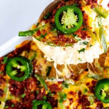 Photo of Jalapeno popper casserole in a white casserole dish garnished with fresh jalapenos with a spoonful being taken out of it with a cheese pull.