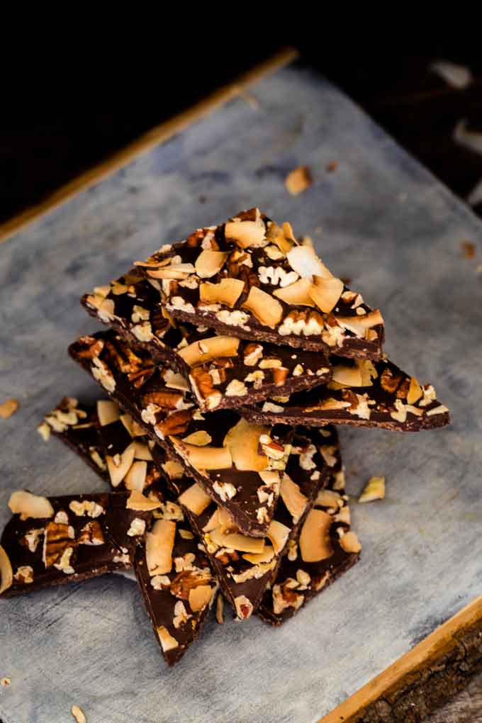 Photo of Keto Chocolate Bark stacked on a rustic cutting board against a dark background.