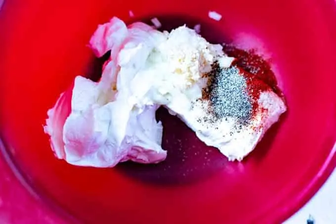 Photo of cream cheese, sour cream, and seasonings in a red bowl.