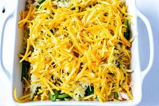 Photo of shredded cheese on top of creamy chicken and jalapenos in a white casserole dish.