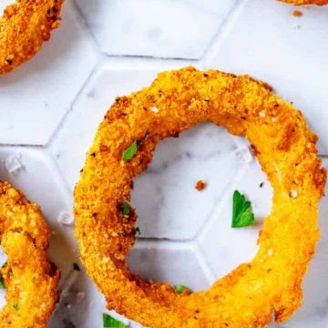 Close up overhead photo of a keto onion ring on a white tile background garnished with parsley and flakey salt.