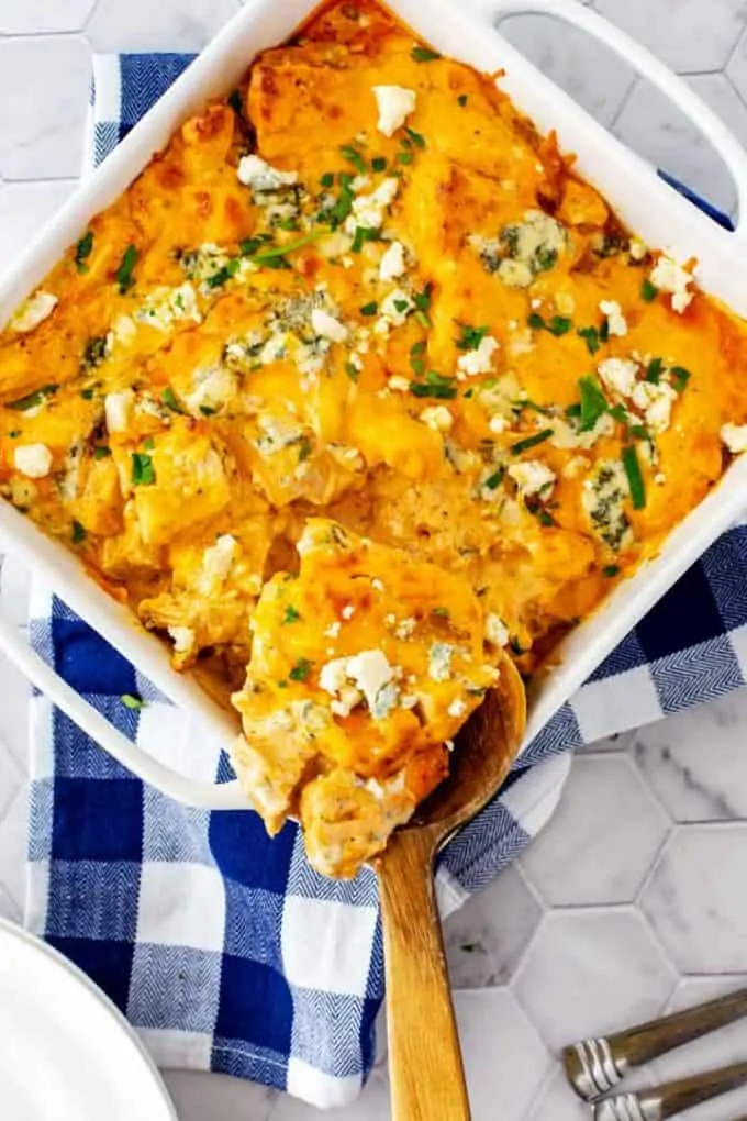 Overhead photo of Keto Buffalo Chicken Casserole with a spoon in a white casserole dish sitting on a blue and white napkin garnished with parsley.