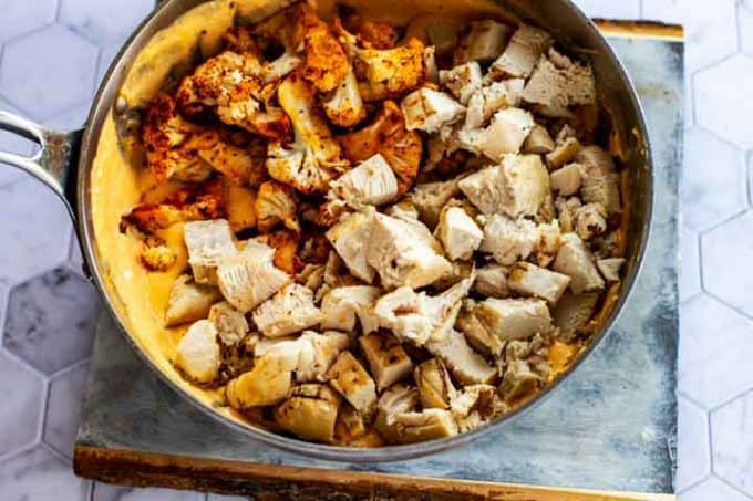 Creamy cheese sauce with roasted cauliflower florets and cubed chicken that has been added on top.