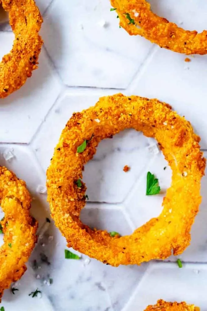Close up overhead photo of a keto onion ring on a white tile background garnished with parsley and flakey salt.