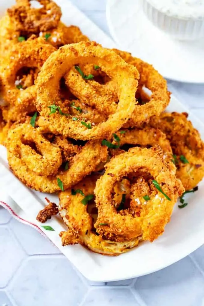 A large white platter with keto onion rings on it sitting on a white tile background.