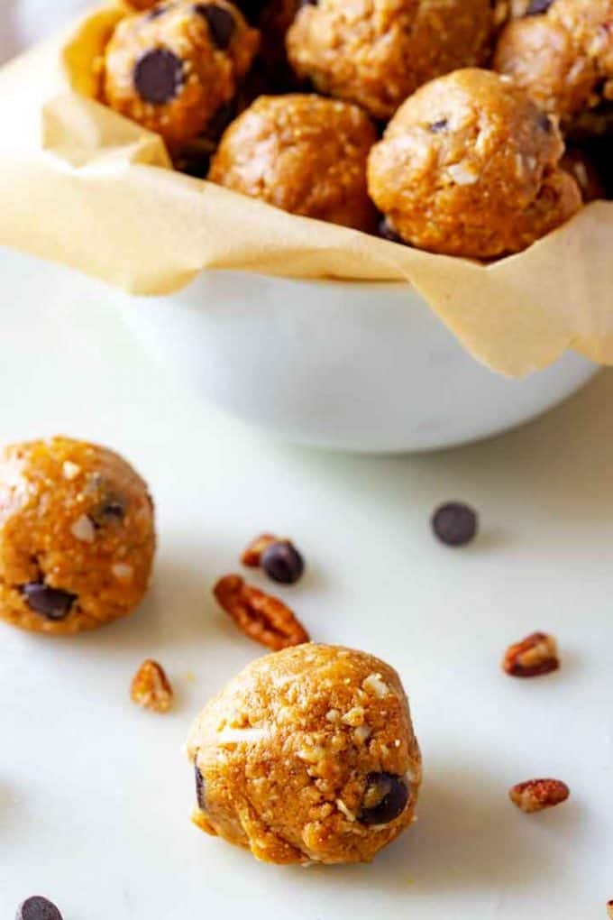 Close up photo of Peanut Butter Chocolate Chip Balls on a white background with a bowl behind it.