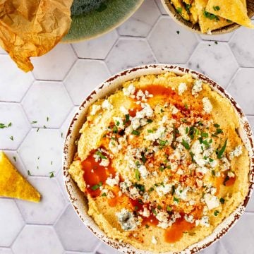 Square overhead photo of Cauliflower Hummus in a rustic bowl against a white tile background with keto tortilla chips next to it.
