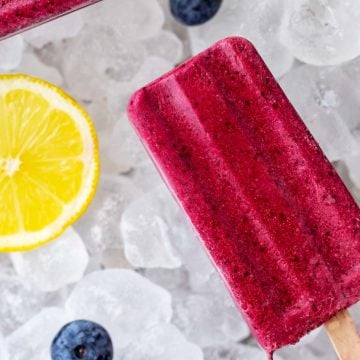Overhead square image of a keto ice pop on a bed of ice with blueberries and a lemon slice next to it.