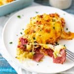 Square photo of a cheesy reuben casserole on a white plate garnished with parsley.