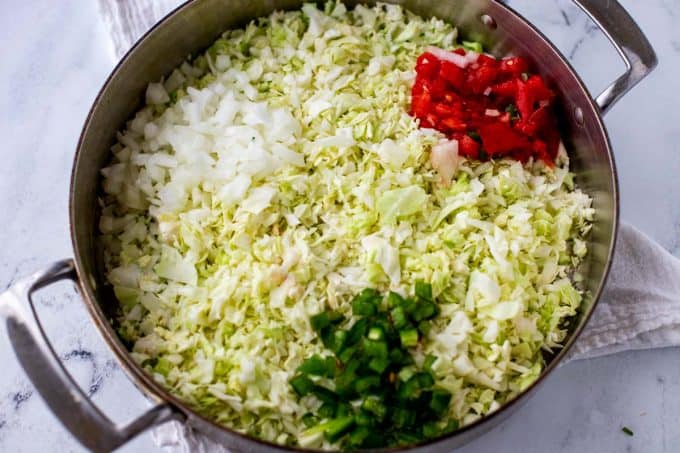 Photo of riced cabbage, tomato and onion in a large skillet.