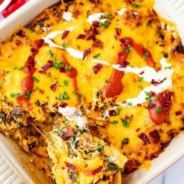 Overhead photo of a cheesy BBQ Chicken Casserole drizzled with ranch dressing and BBQ sauce with a spoon coming from it.