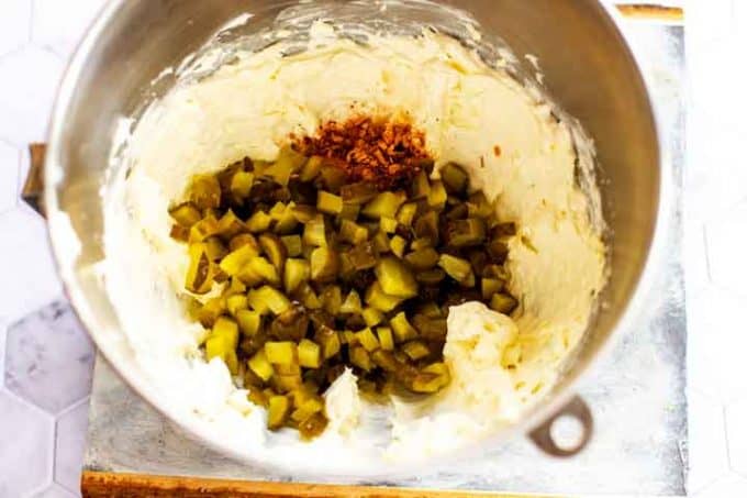 Photo of pickles and seasonings being added to a cream cheese based dip.