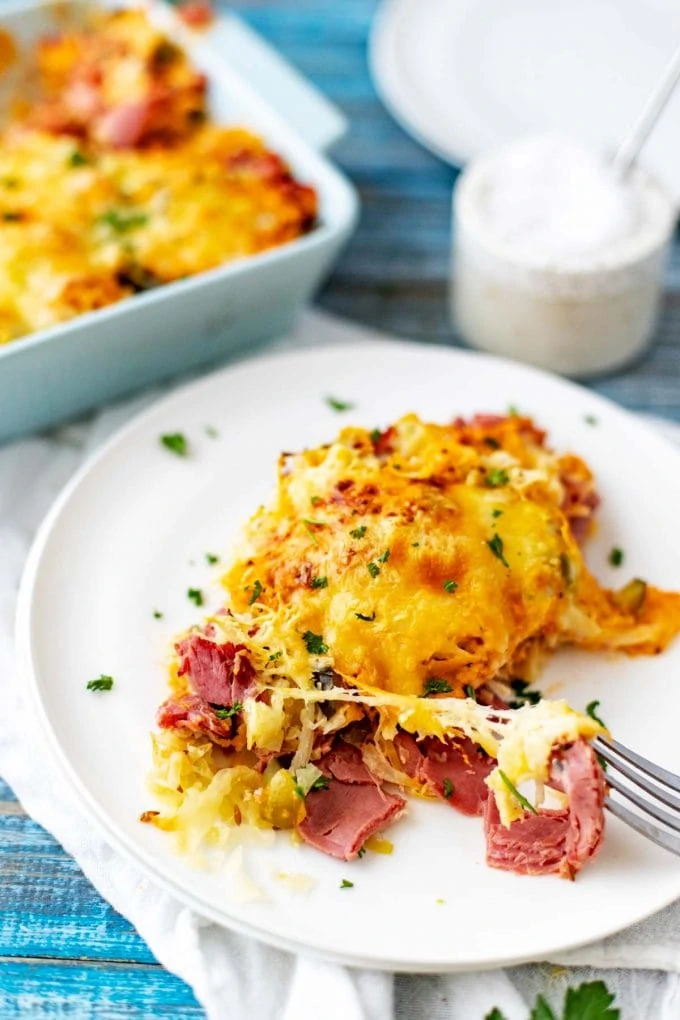 Photo of a Keto Reuben Casserole on a white plate with fork pulling a cheesy bite from it.