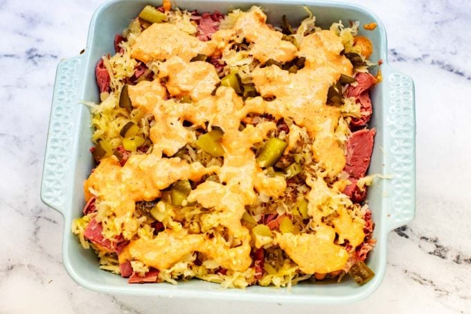 Photo of a mixture of Photo of mayonnaise, cream cheese, ketchup, horseradish, paprika, salt, and pepper that has been drizzled over corned beef, chopped pickles sauerkraut, and caraway seeds.