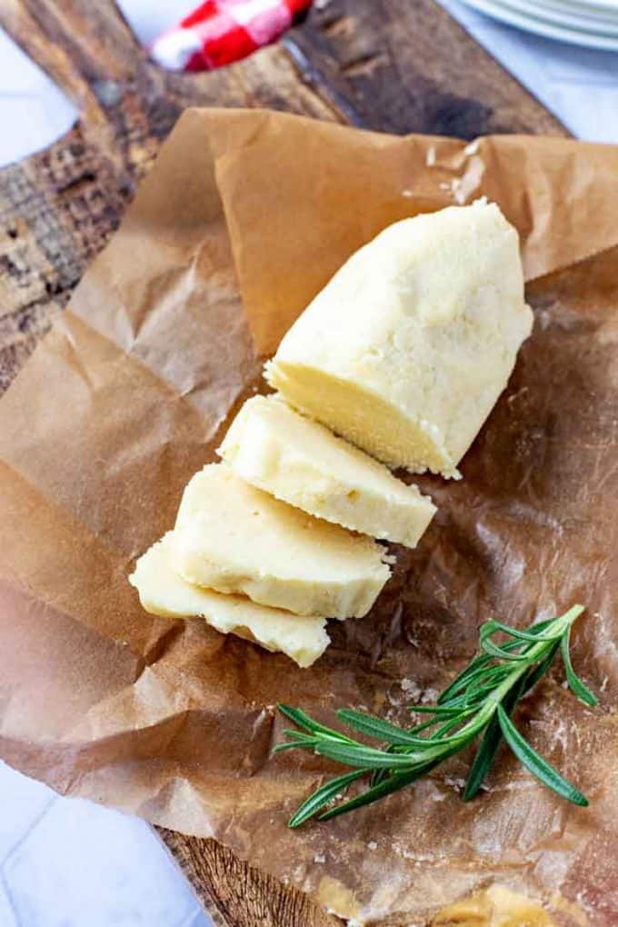 Photo of a log of parmesan butter sitting on a parchment lined cutting board with a piece of fresh rosemary next to it.
