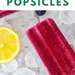 Overhead photo of one full and one partial Keto Popsicle on a bed of ice surrounded by lemon slices and fresh blueberries with the text easy keto popsicles above.