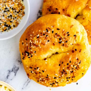 Close up square photo of keto fathead bagels on a white background with a small dish of everything seasoning next to it.