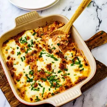 Square photo of Keto Chicken Parmesan Casserole in a casserole dish with with wooden spoon.