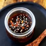Close up square photo of keto teriyaki sauce in a small glass jar garnished with red pepper flakes and sesame seeds.