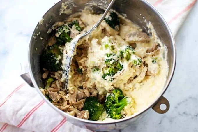 Photo of chicken and broccoli being mixed with alfredo sauce in a large bowl.