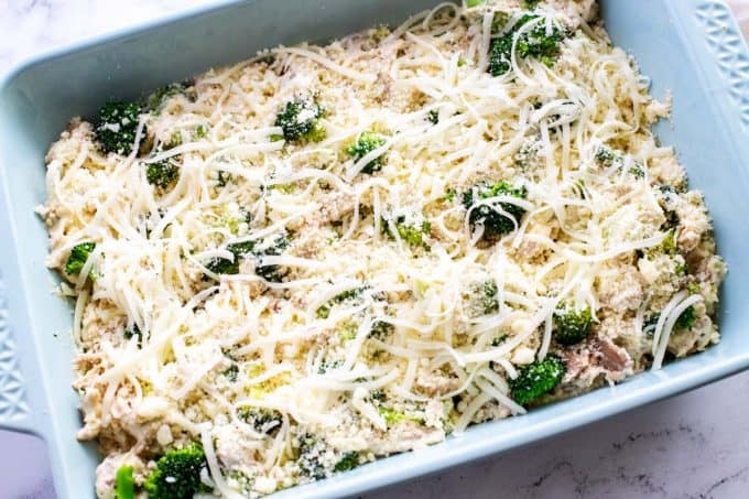 Photo of a light blue casserole dish with chicken and broccoli that have been tossed with alfredo sauce and topped with parmesan and mozzarella cheese.
