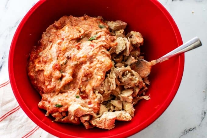 Photo of ricotta cheese and marinara mixed together sitting on top of chicken in a red bowl.